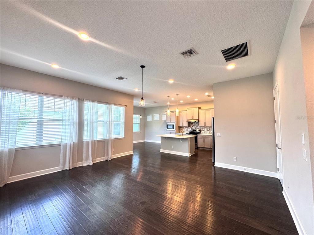 An open-concept living area features dark hardwood floors, light gray walls, and a modern kitchen — 13808 CHAUVIN AVENUE, ORLANDO, FL