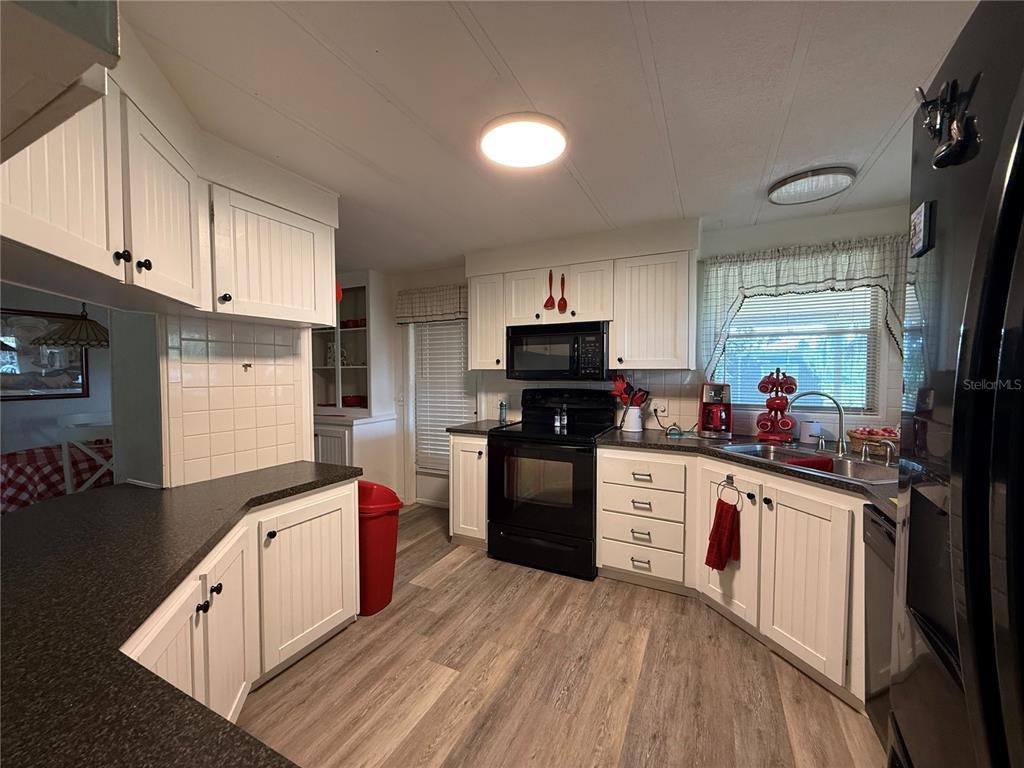 A kitchen features white cabinets, dark countertops, black appliances, and light wood-look flooring — 24 N BOBWHITE ROAD, WILDWOOD, FL