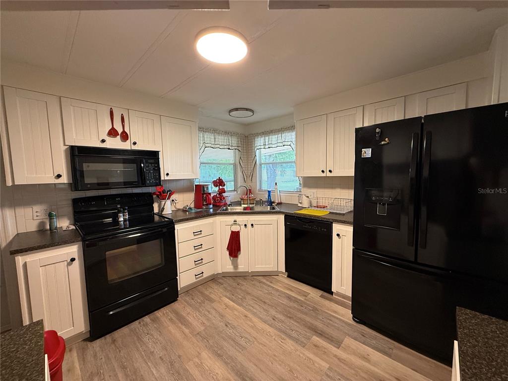 A kitchen features white cabinets, black appliances, a corner sink, and wood-look flooring — 24 N BOBWHITE ROAD, WILDWOOD, FL