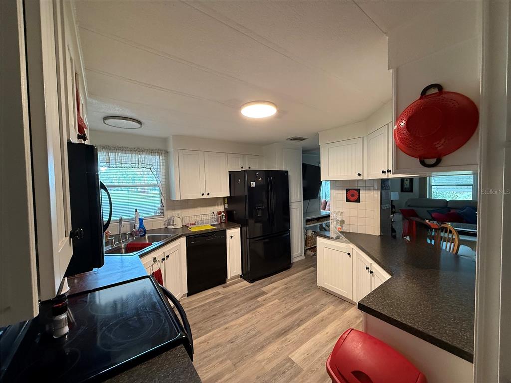 A kitchen features white cabinets, black appliances, dark countertops, and light wood-look flooring — 24 N BOBWHITE ROAD, WILDWOOD, FL