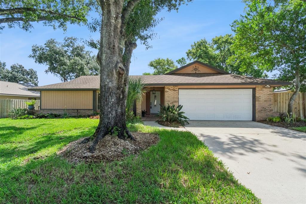 A single-story house with a brick and wood exterior, a two-car garage, and a large tree — 1591 KENLYN DRIVE, LONGWOOD, FL