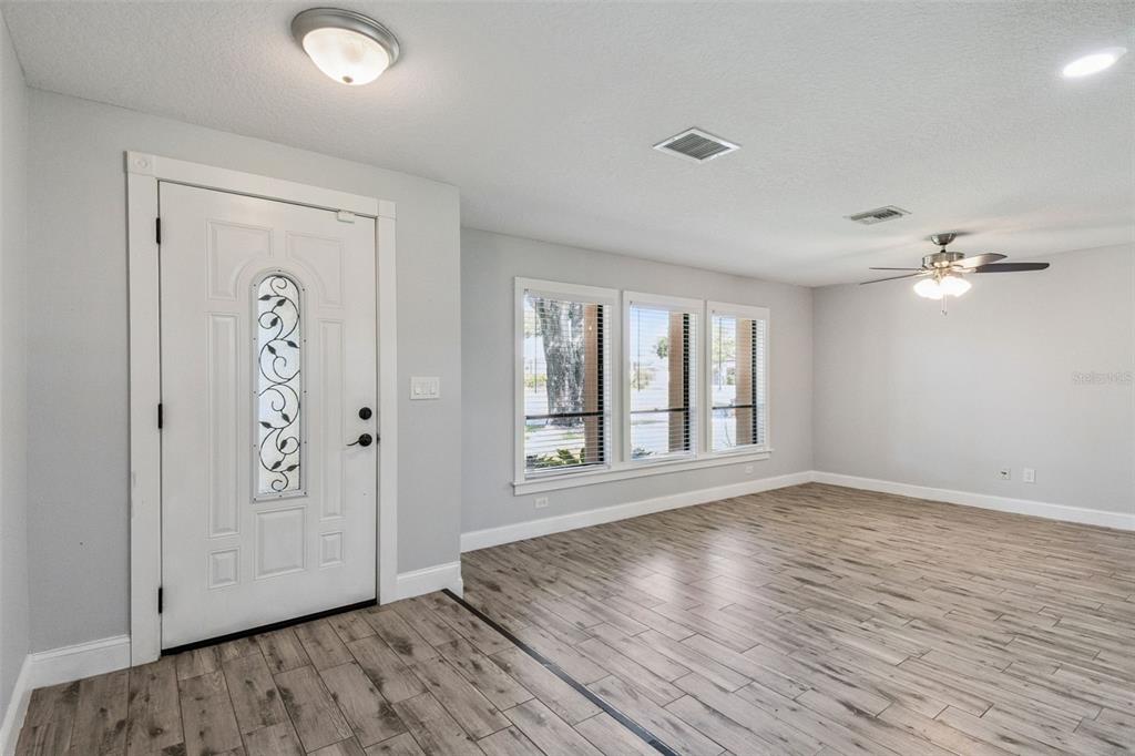 A bright living room features light gray walls, wood-look tile flooring, and a front door — 1591 KENLYN DRIVE, LONGWOOD, FL