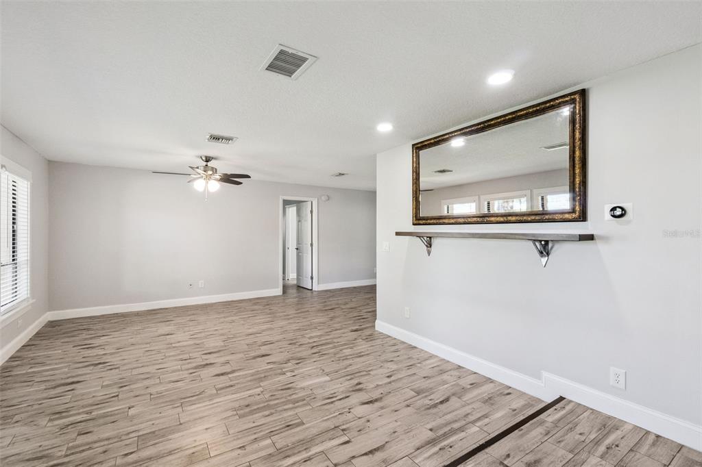 A living room features light gray walls, wood-look tile flooring, a ceiling fan, and a mirror — 1591 KENLYN DRIVE, LONGWOOD, FL