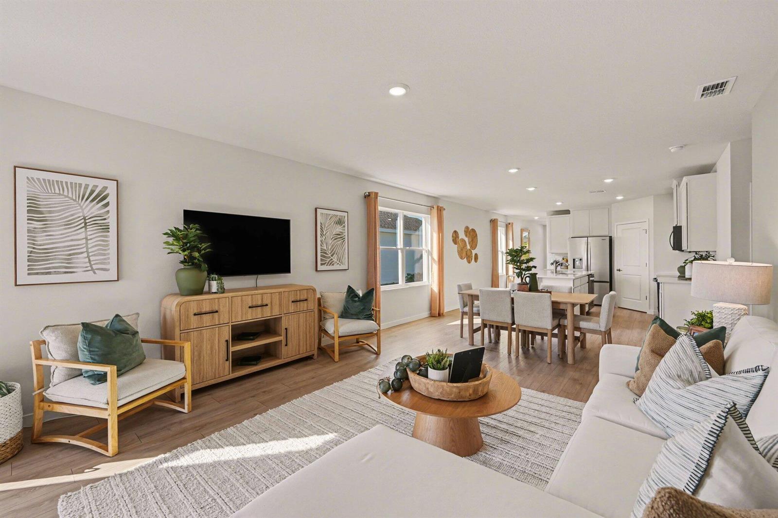 A bright, open-concept living and dining area features light wood flooring, a white sofa, and kitchen — 9633 Venetian Square, Vero Beach FL 32966, VERO BEACH, FL