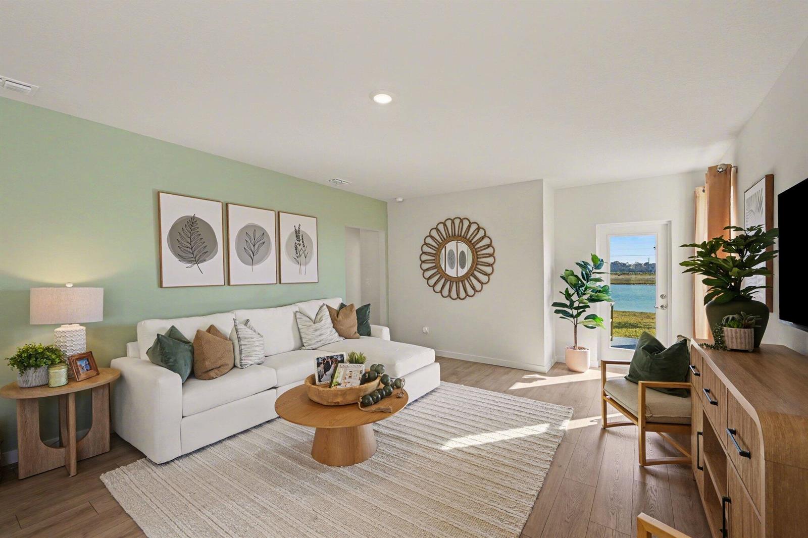 A living room features a white sectional sofa, sage green accent wall, and water view — 9633 Venetian Square, Vero Beach FL 32966, VERO BEACH, FL