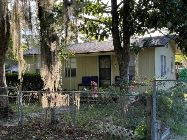 A single-story house with light yellow siding and a dark roof behind a chain-link fence — 917 NE 25TH STREET, GAINESVILLE, FL