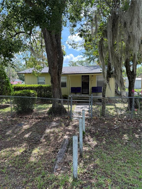 A yellow single-story house with a chain-link fence and large trees in the front yard — 917 NE 25TH STREET, GAINESVILLE, FL
