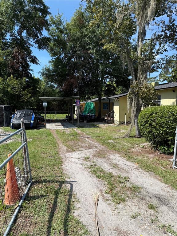 A dirt driveway leads to a yellow house with a carport and a covered vehicle — 917 NE 25TH STREET, GAINESVILLE, FL