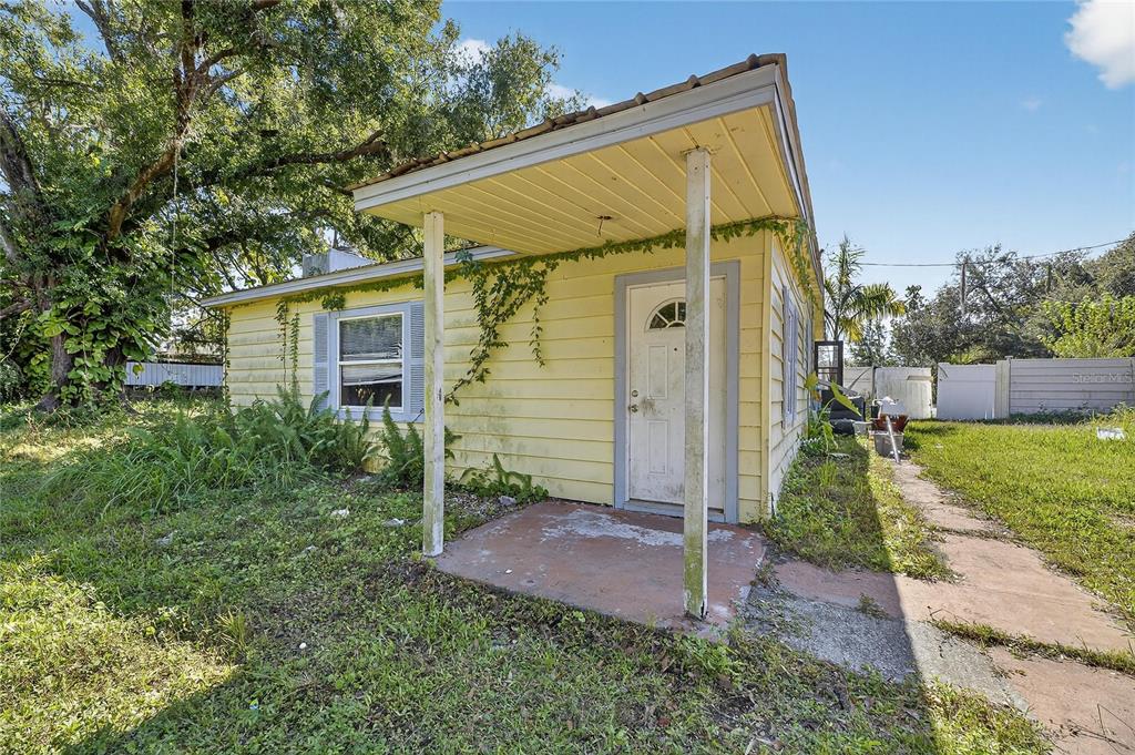 A small, yellow, single-story house with a covered front porch and overgrown landscaping — 311 S WEBB ROAD, PLANT CITY, FL