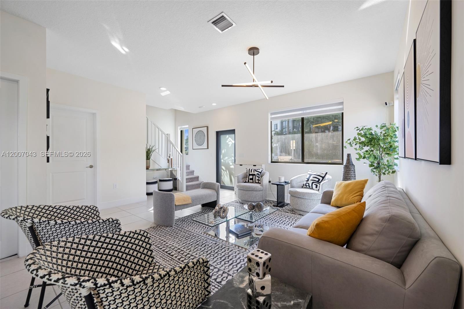 A modern living room features a grey sofa, patterned armchairs, a glass coffee table, and stairs — 8387 NW 43rd St, Doral FL 33166, DORAL, FL