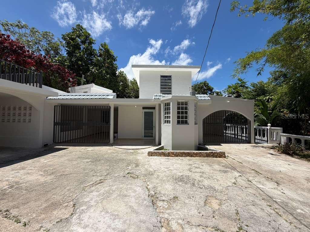 A white two-story house with a concrete driveway, gated carports, and a stone planter — 8 Martorell MARTORELL, YABUCOA, PR