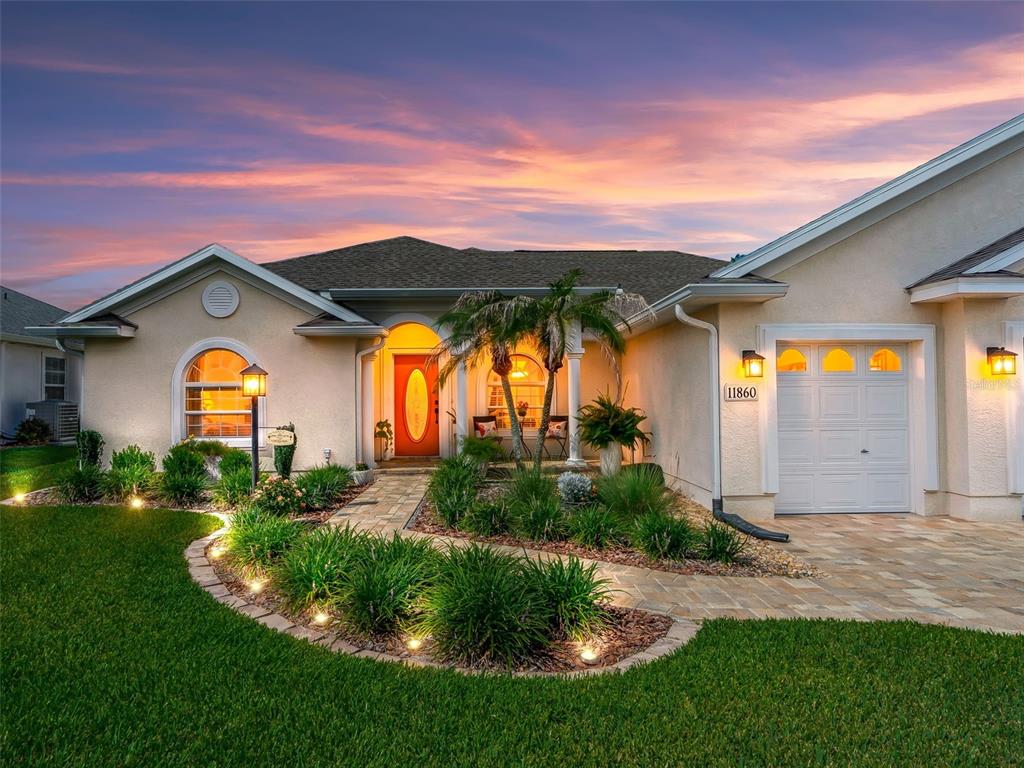 A single-story house with a paved walkway, landscaped garden, and a garage at sunset — 11860 SE 179TH STREET, SUMMERFIELD, FL