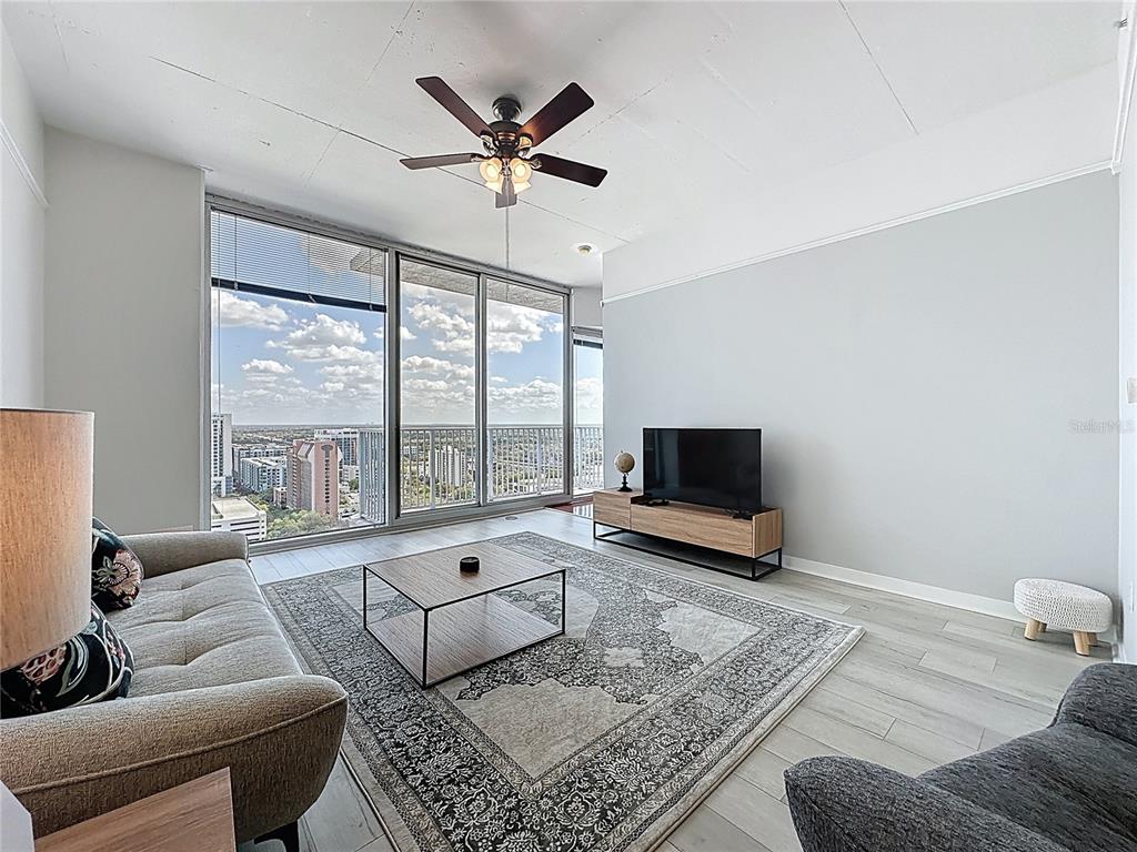 A living room features a sofa, coffee table, television, and floor-to-ceiling windows overlooking a city — 155 S COURT AVENUE UNIT 1911, ORLANDO, FL