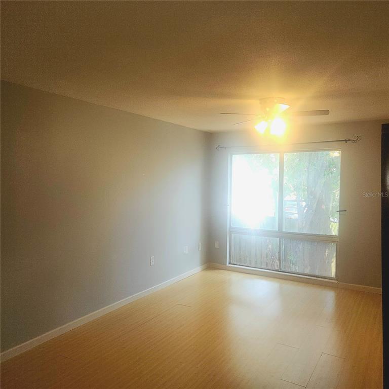 An empty room with light-colored walls, wood-look flooring, a ceiling fan, and a large window — 1700 SW 16TH COURT UNIT P28, GAINESVILLE, FL