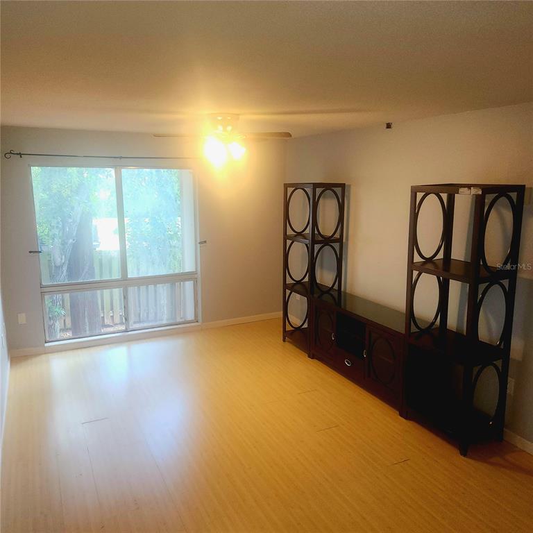 A living room with light wood flooring, a large window, and a dark media console — 1700 SW 16TH COURT UNIT P28, GAINESVILLE, FL