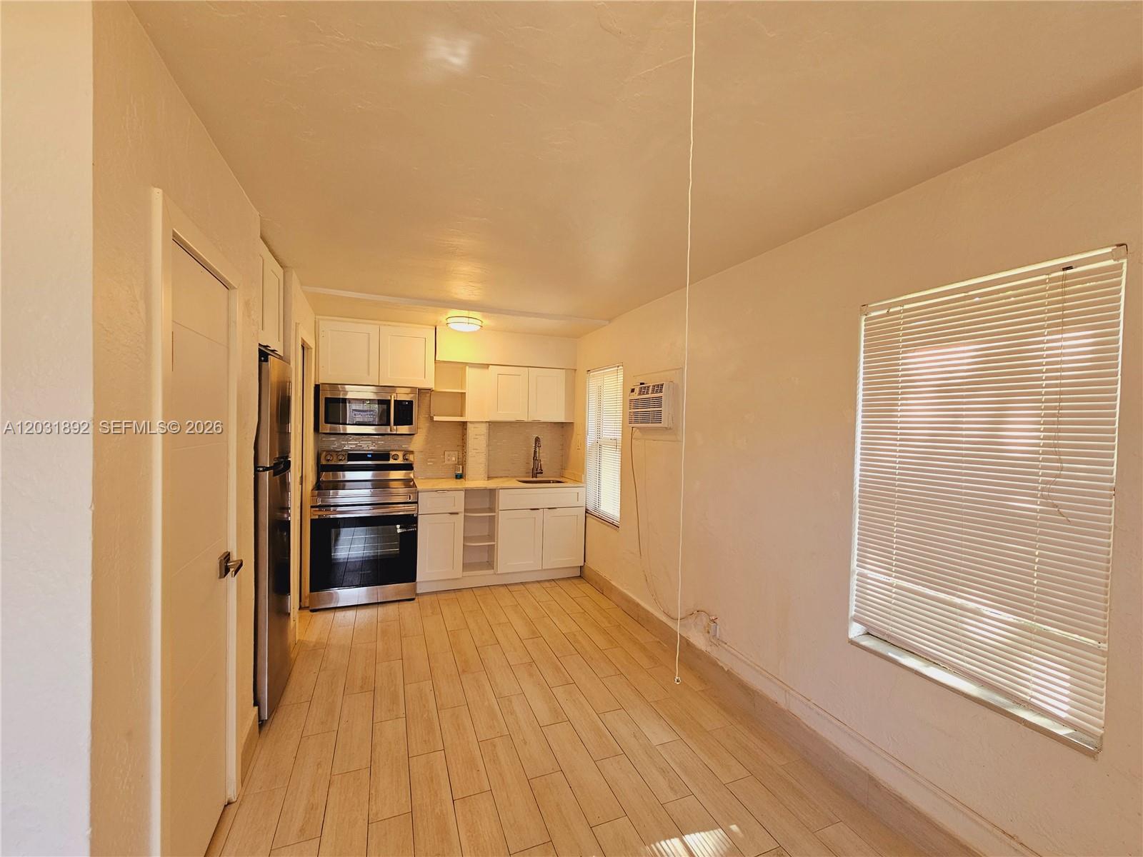 A small kitchen features white cabinets, stainless steel appliances, and light wood-look tile flooring — 26 SE 13th Ter # 6, Dania Beach FL 33004, DANIA BEACH, FL