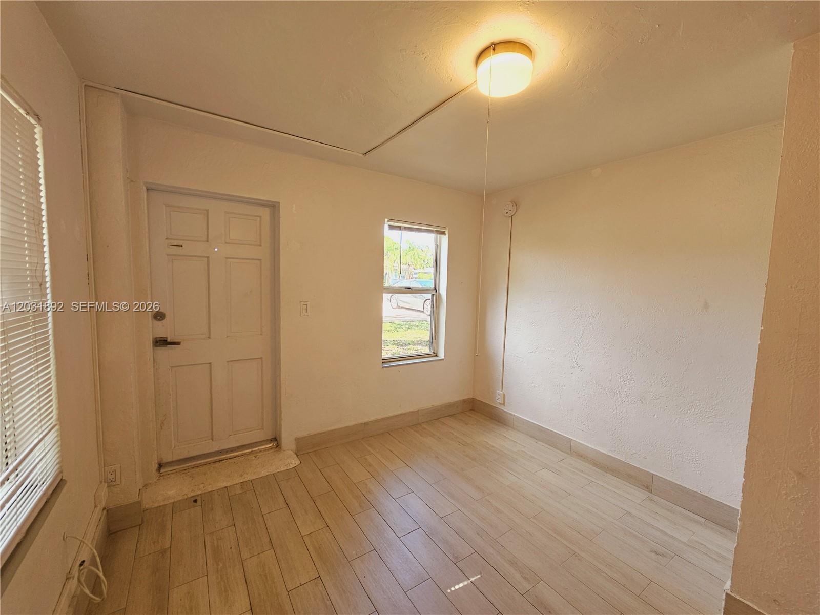 A small room features white walls, light wood-look tile flooring, a door, and a window — 26 SE 13th Ter # 6, Dania Beach FL 33004, DANIA BEACH, FL