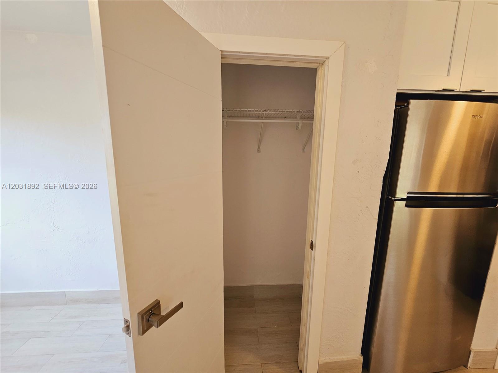 A white door opens to a small closet with a wire shelf next to a refrigerator — 26 SE 13th Ter # 6, Dania Beach FL 33004, DANIA BEACH, FL