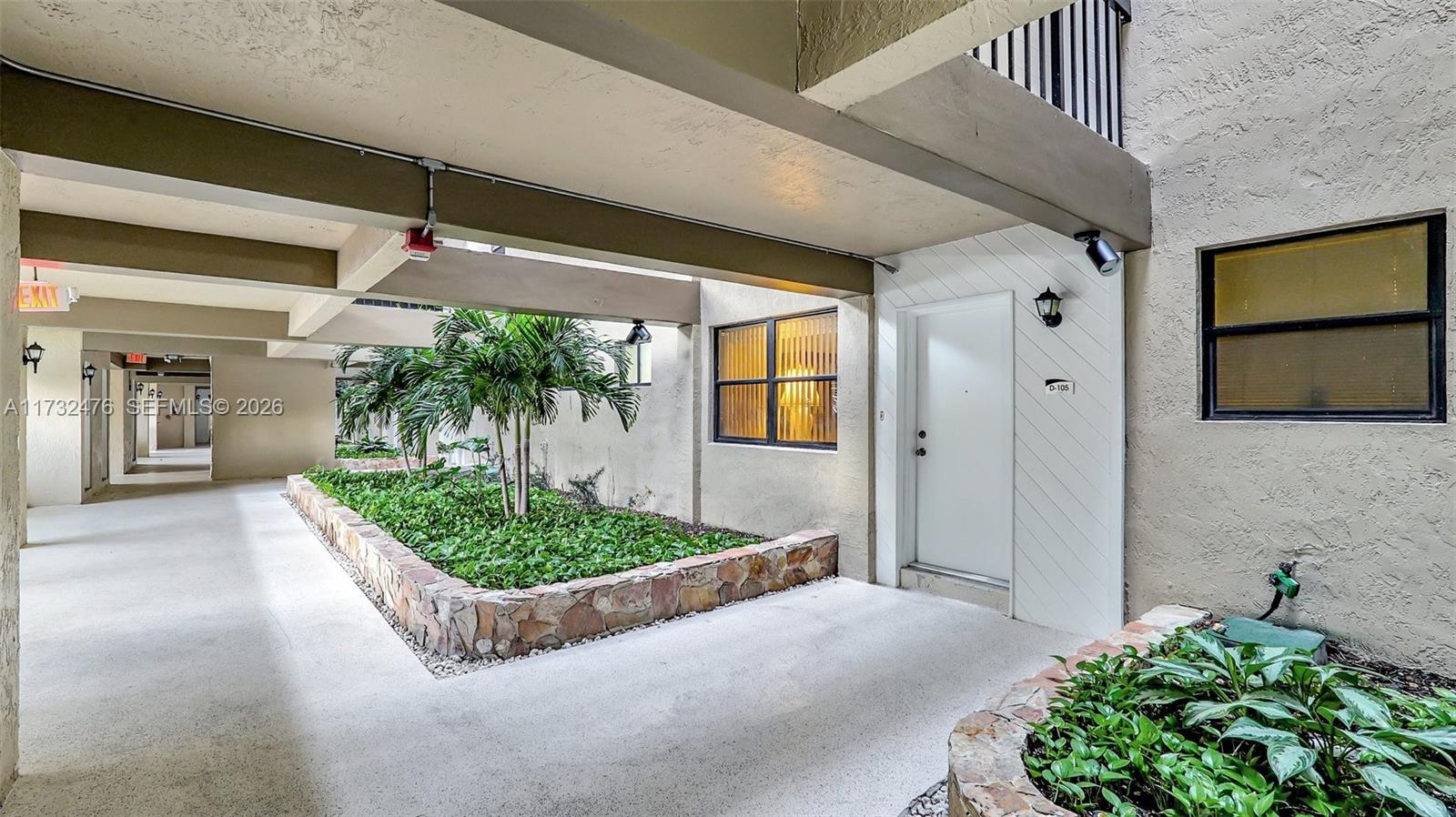 An outdoor walkway features a stone-bordered garden bed with palm trees and a white door — 481 Ives Dairy Rd # 4, Miami FL 33179, MIAMI, FL