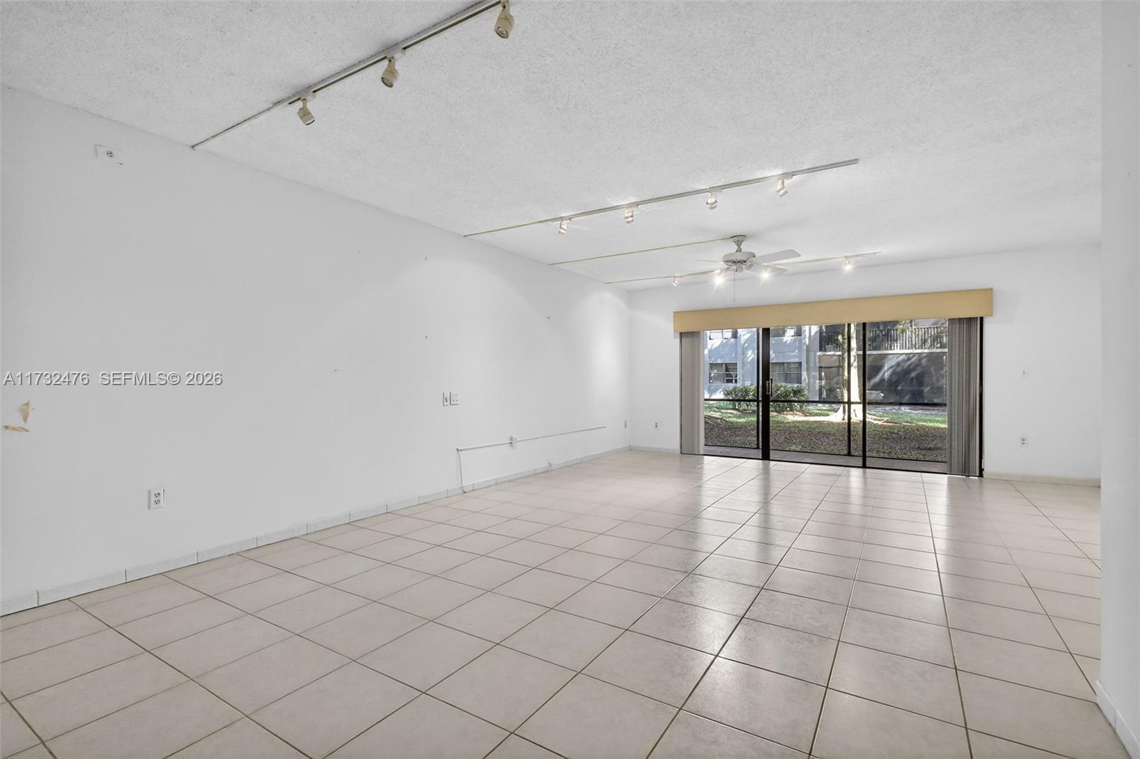 An empty room features white walls, tile flooring, track lighting, and a sliding glass door — 481 Ives Dairy Rd # 4, Miami FL 33179, MIAMI, FL