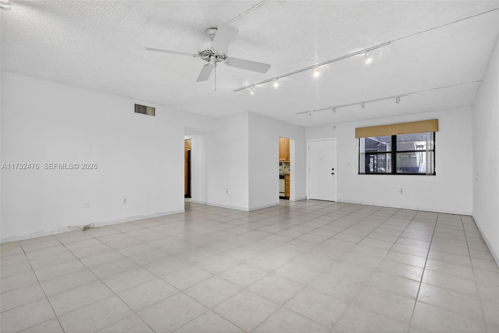 A spacious, white-walled living room features light-colored tile flooring, a ceiling fan, and track lighting — 481 Ives Dairy Rd # 4, Miami FL 33179, MIAMI, FL