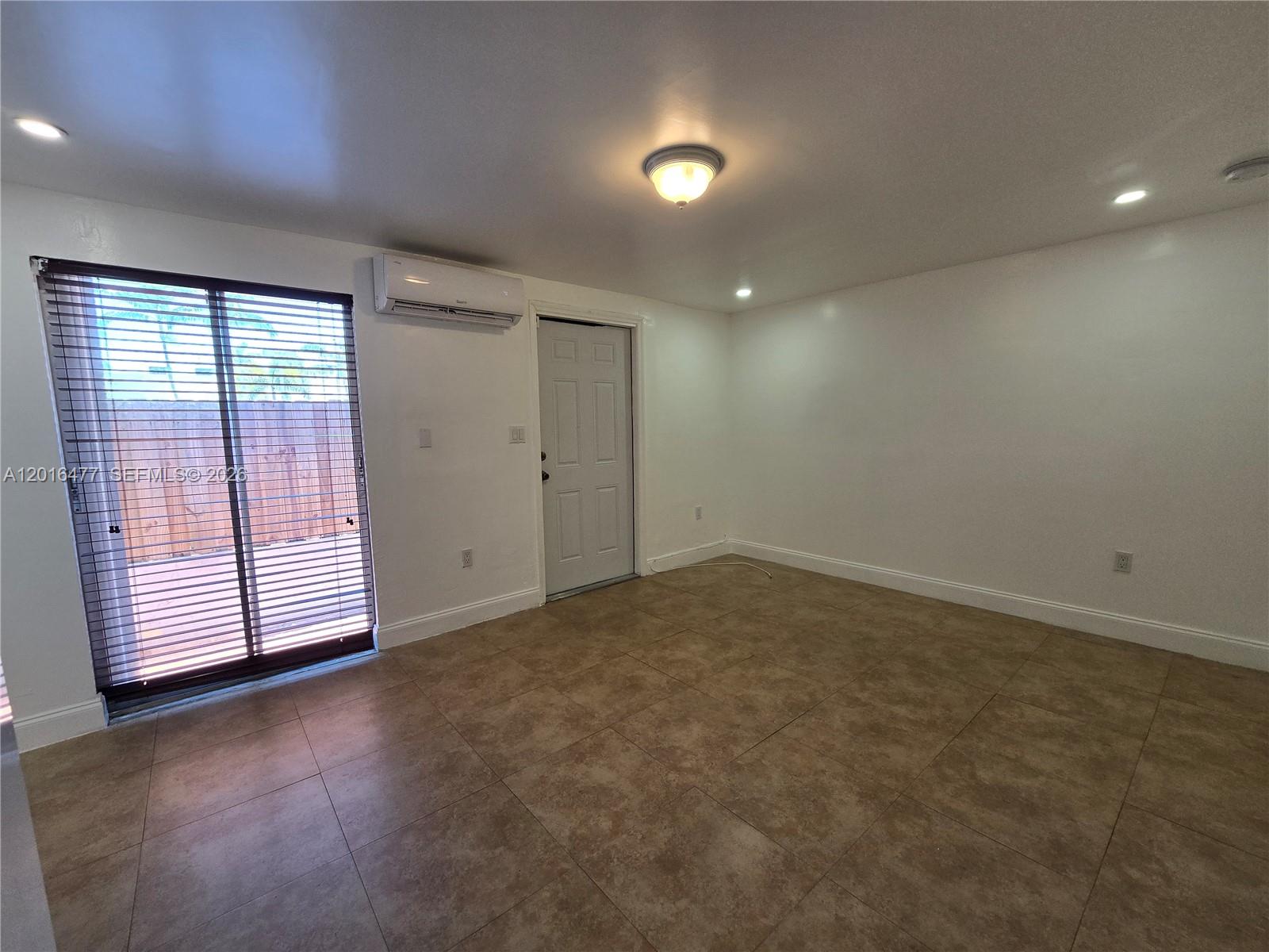 An empty room with tan tile flooring, white walls, a sliding glass door, and a mini-split — 2957 SW 36th Ct # 4, Miami FL 33133, MIAMI, FL