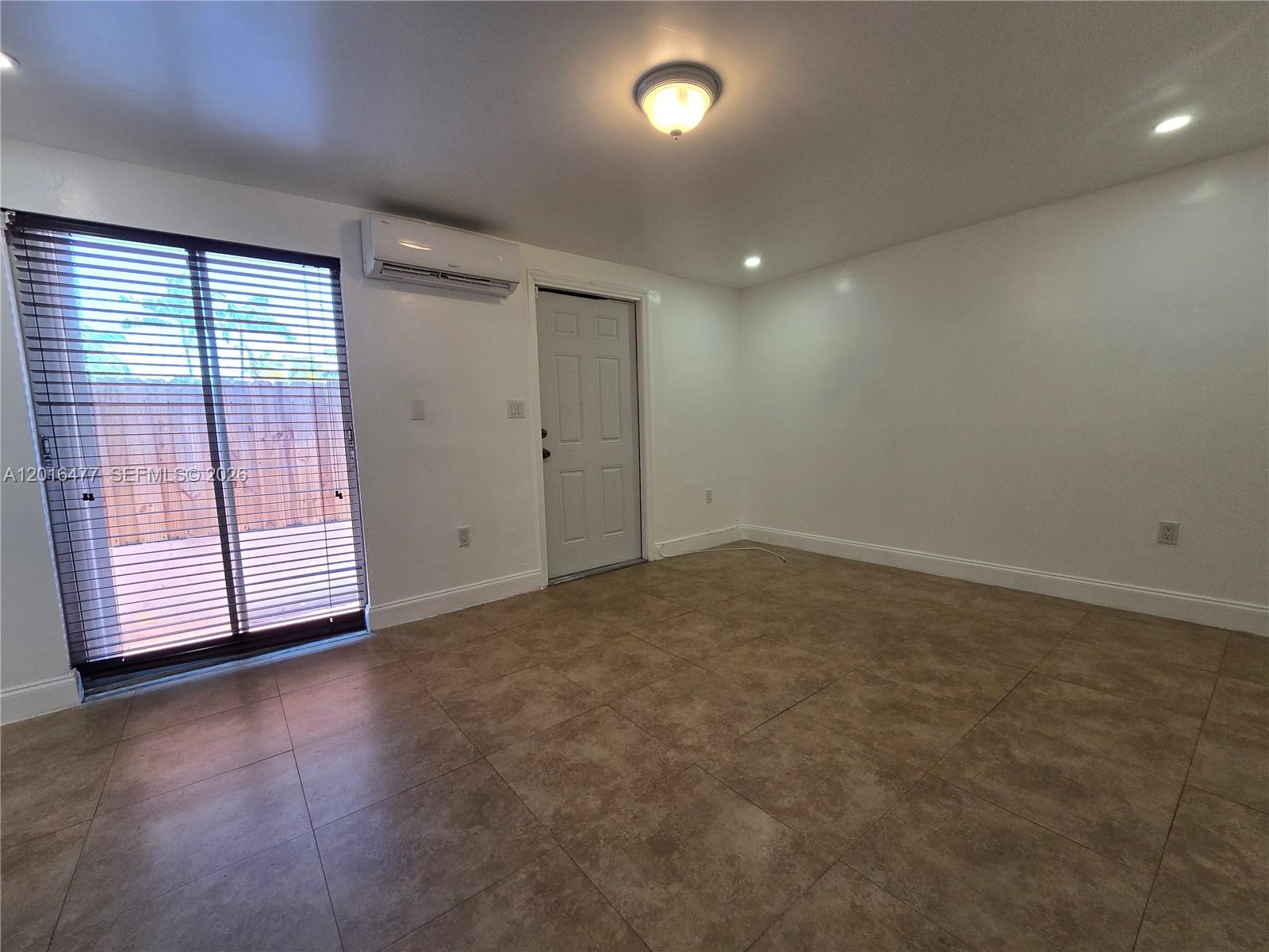 An empty room features tile flooring, white walls, a sliding glass door, and a wall-mounted AC — 2957 SW 36th Ct # 4, Miami FL 33133, MIAMI, FL