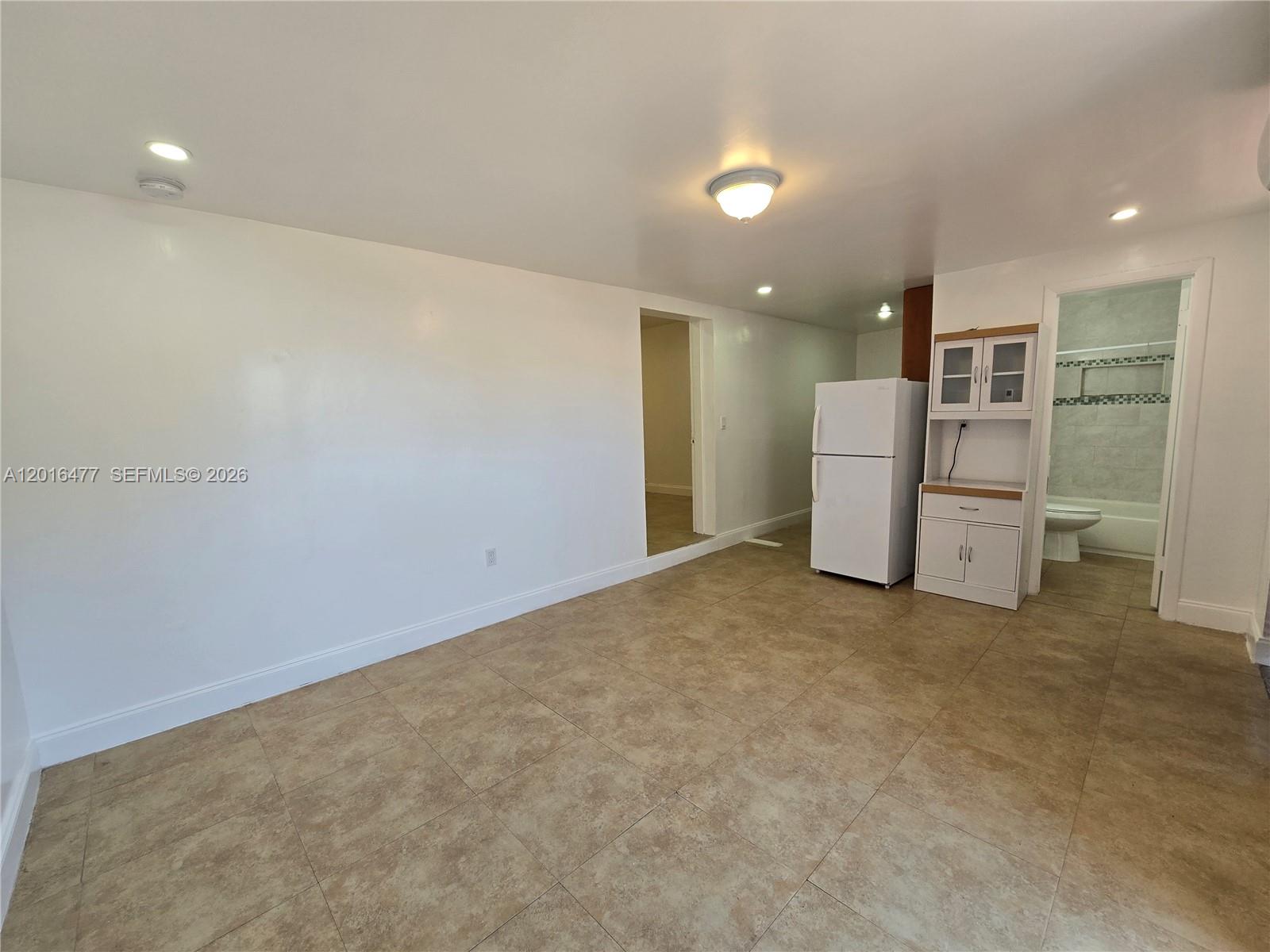 A room with beige tile flooring, a white refrigerator, a small cabinet, and a bathroom — 2957 SW 36th Ct # 4, Miami FL 33133, MIAMI, FL