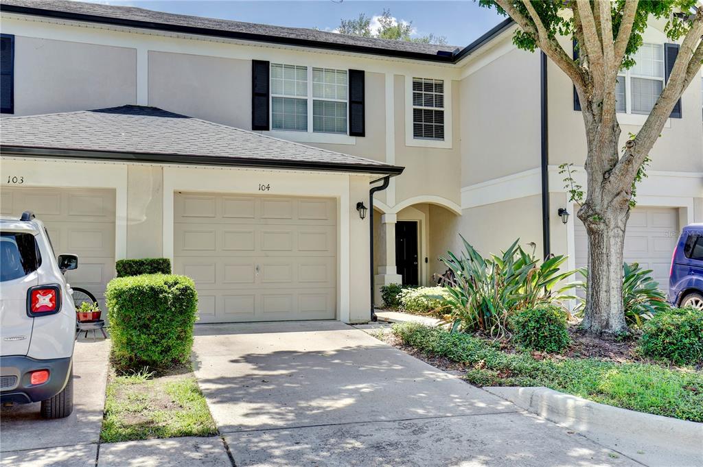 The exterior of a two-story townhouse features a beige garage, a front entrance, and landscaping — 6080 TWAIN STREET UNIT 104, ORLANDO, FL