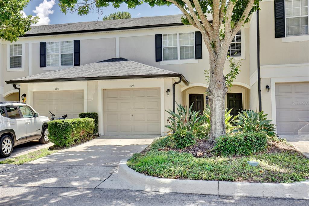 A two-story townhouse exterior features a beige facade, garage doors, and a landscaped front yard — 6080 TWAIN STREET UNIT 104, ORLANDO, FL