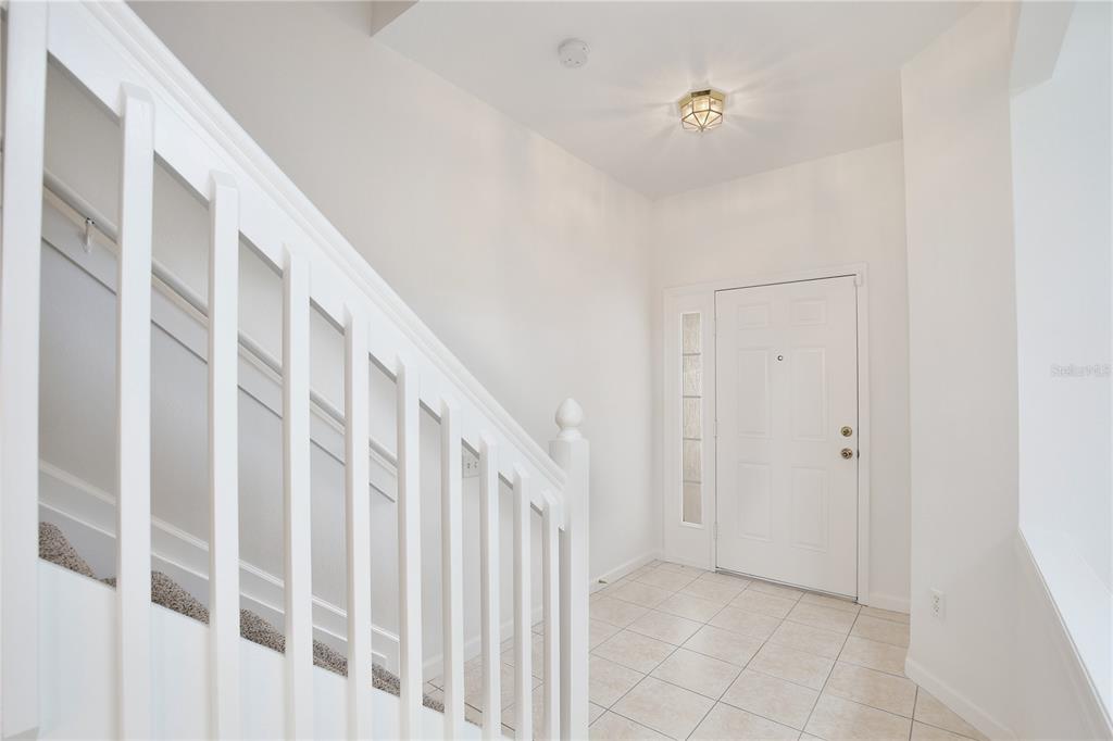 An entryway with white walls, tile flooring, a staircase with white railings, and a front door — 6080 TWAIN STREET UNIT 104, ORLANDO, FL