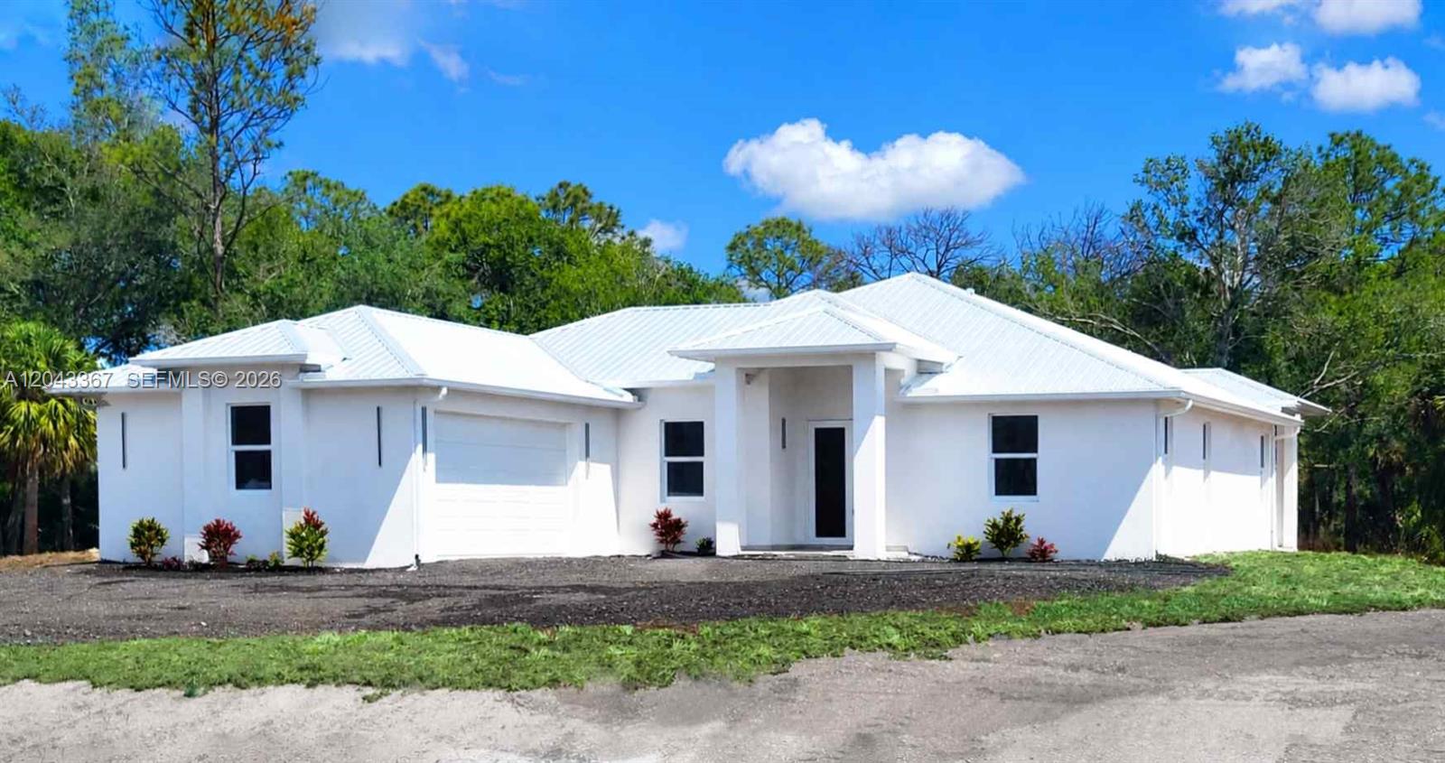 A white, single-story house with a metal roof and a garage sits on a lot — 133 Hunting Club Ave, Clewiston FL 33440, CLEWISTON, FL