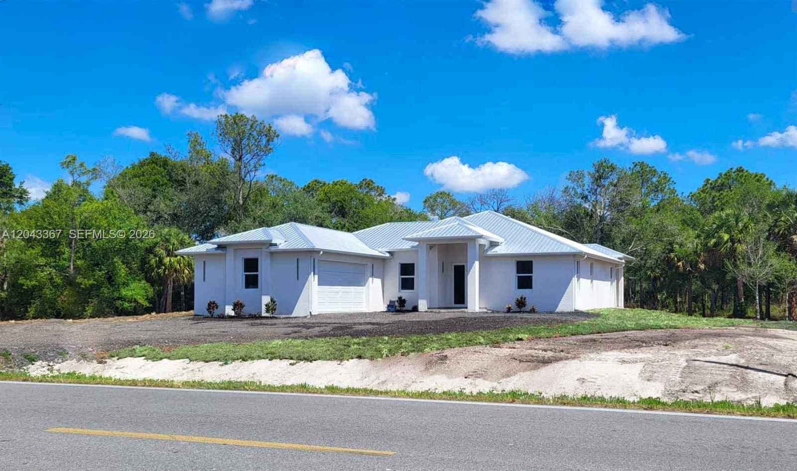 A white, single-story house with a metal roof sits on a grassy lot — 133 Hunting Club Ave, Clewiston FL 33440, CLEWISTON, FL