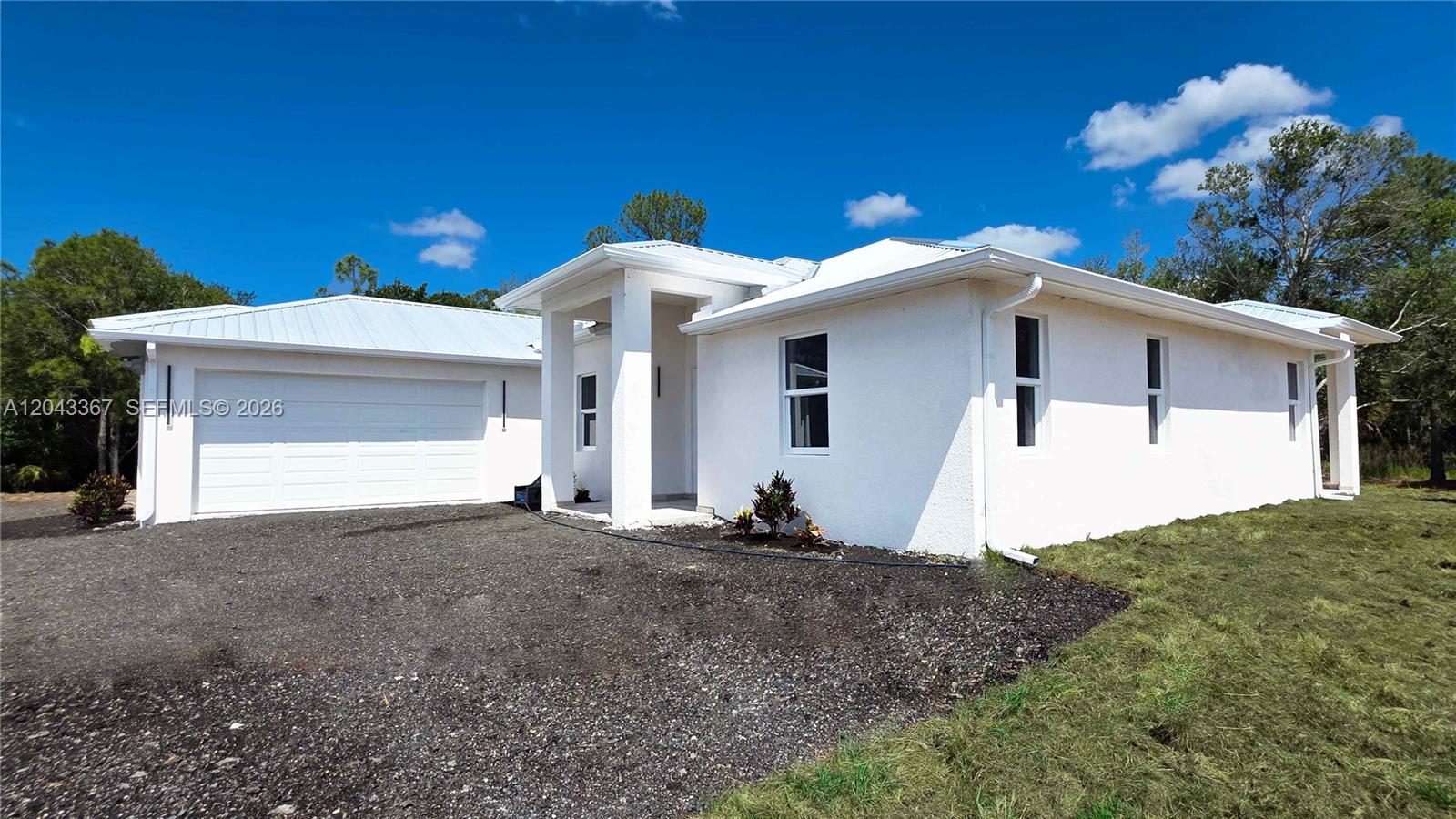 A white, single-story house with a metal roof and a two-car garage — 133 Hunting Club Ave, Clewiston FL 33440, CLEWISTON, FL