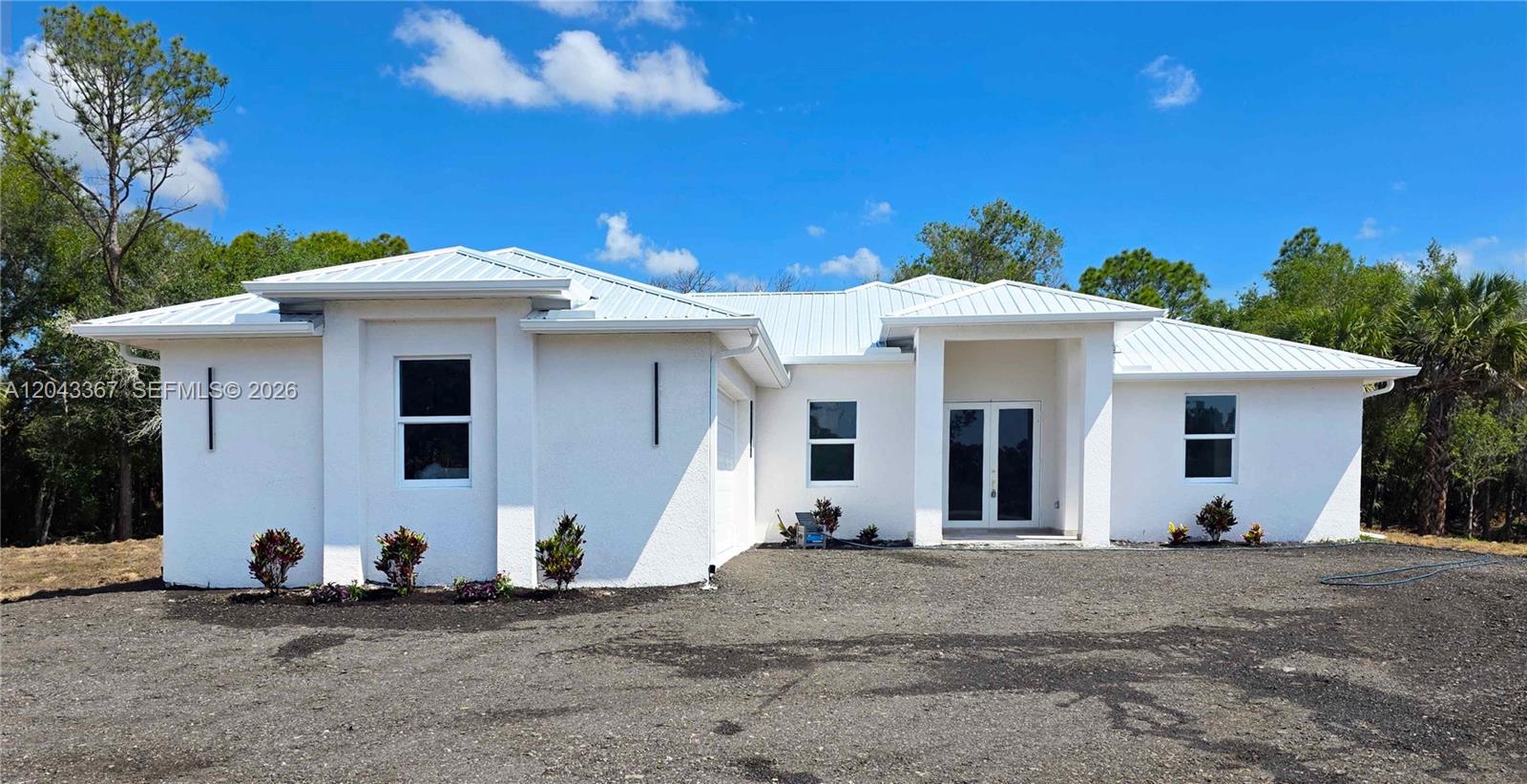 A white, single-story house with a metal roof sits on a gravel lot — 133 Hunting Club Ave, Clewiston FL 33440, CLEWISTON, FL