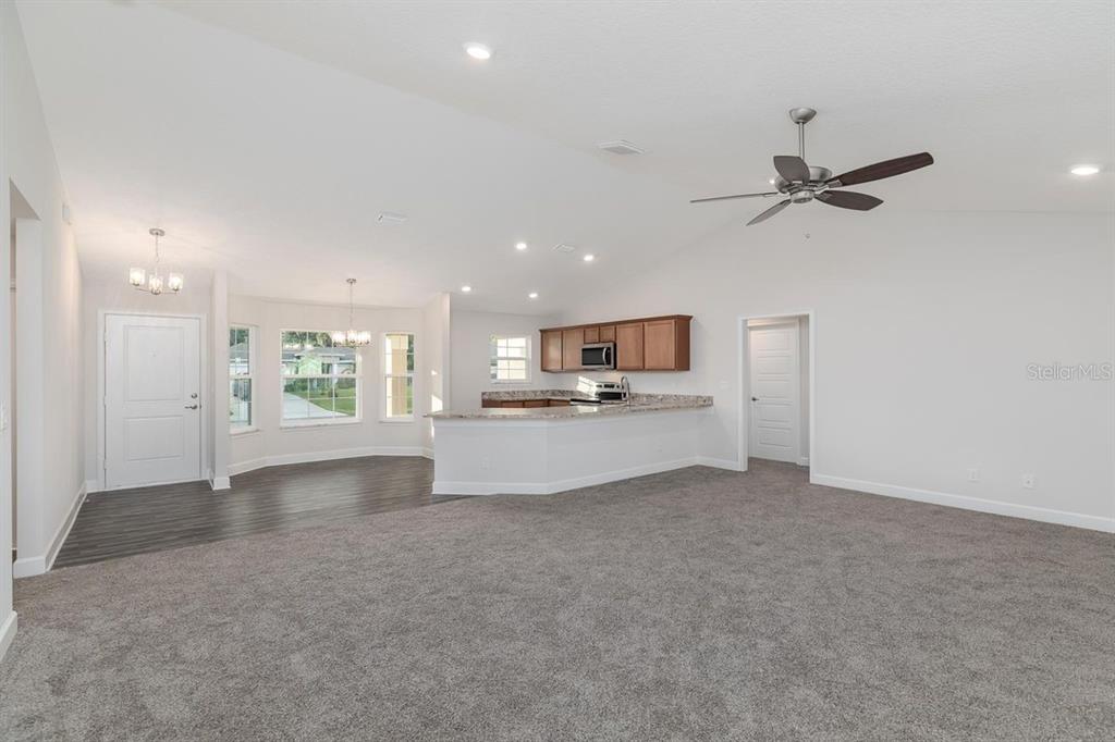 An open-concept living area features gray carpeting, a kitchen with wood cabinets, and a dining nook — 53 SLEEPY HOLLOW TRAIL, PALM COAST, FL