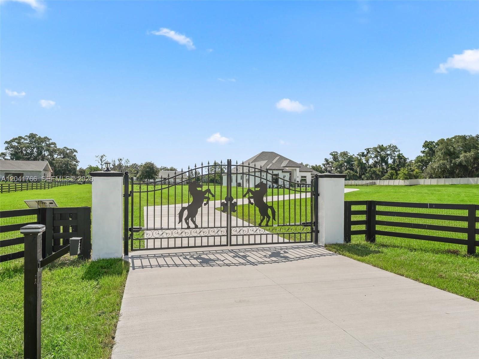 A black metal gate with horse silhouettes stands at the entrance of a grassy property — 7041 NE 22nd Court Rd, Ocala FL 34479, OCALA, FL