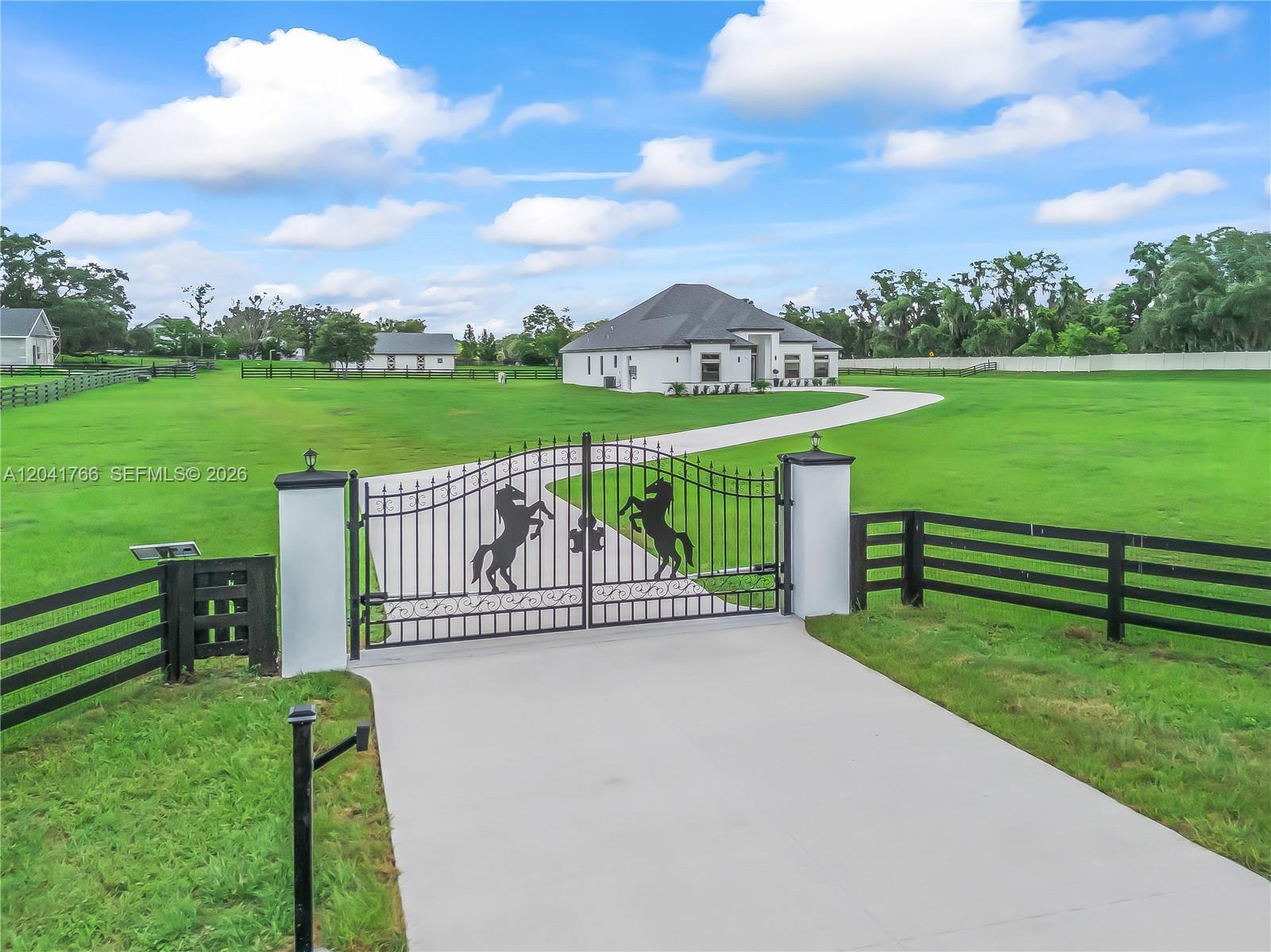A gated driveway leads to a white house on a large, grassy rural property — 7041 NE 22nd Court Rd, Ocala FL 34479, OCALA, FL