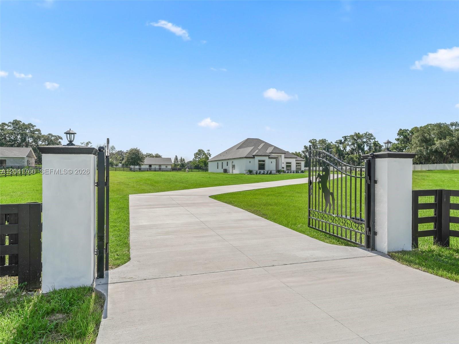 A concrete driveway leads through an open gate toward a white house on a lawn — 7041 NE 22nd Court Rd, Ocala FL 34479, OCALA, FL