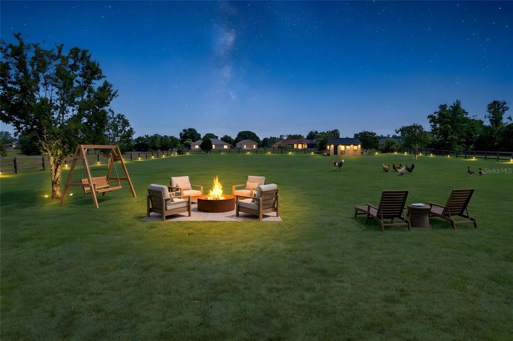 A backyard at night features a fire pit, seating area, and a small wooden shed — 10064 SW 98TH LANE, GAINESVILLE, FL