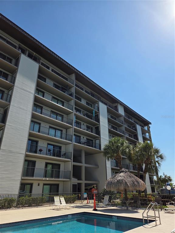 A multi-story apartment building with balconies overlooks a swimming pool and a thatched umbrella — 650 ISLAND WAY UNIT 202, CLEARWATER BEACH, FL