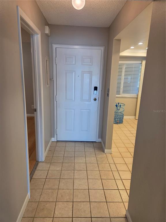An entryway with light-colored tile flooring, a white front door, and a doorway to the left — 650 ISLAND WAY UNIT 202, CLEARWATER BEACH, FL