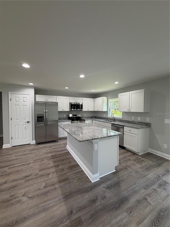 A modern kitchen features white cabinets, granite countertops, a center island, and wood-look flooring — 1987 LEMON DRIVE, LAKE WALES, FL