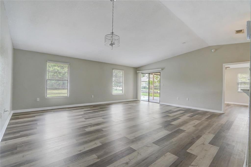 A spacious living room features light gray walls, wood-look plank flooring, and a hanging chandelier — 104 TURIN WAY, KISSIMMEE, FL