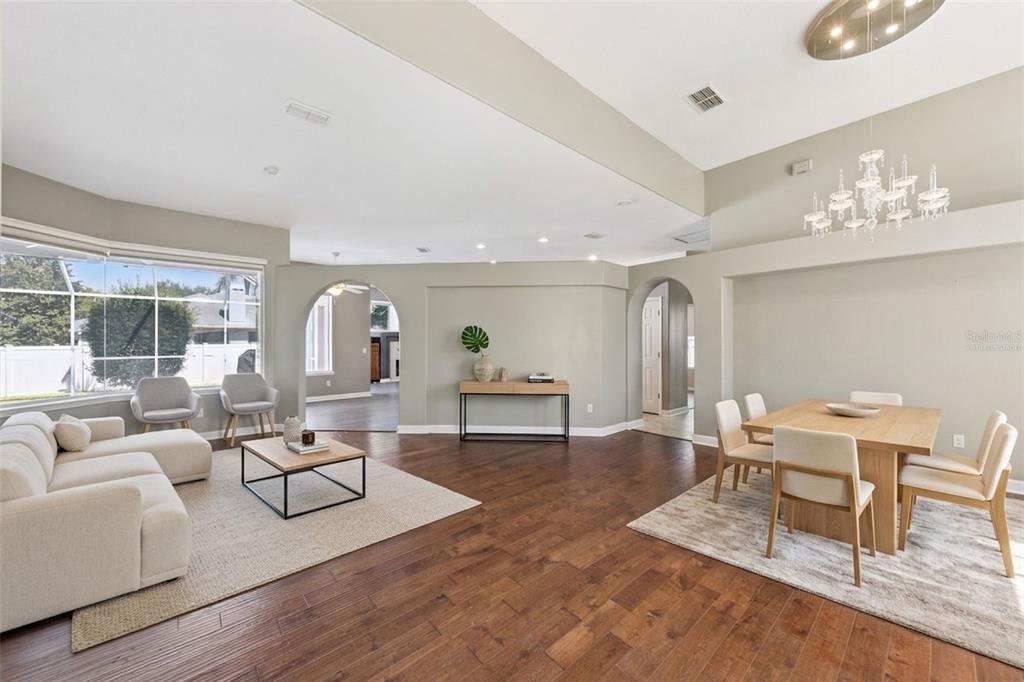 An open-concept living and dining area with hardwood floors, arched doorways, and a crystal chandelier — 8041 MONIER WAY, ORLANDO, FL
