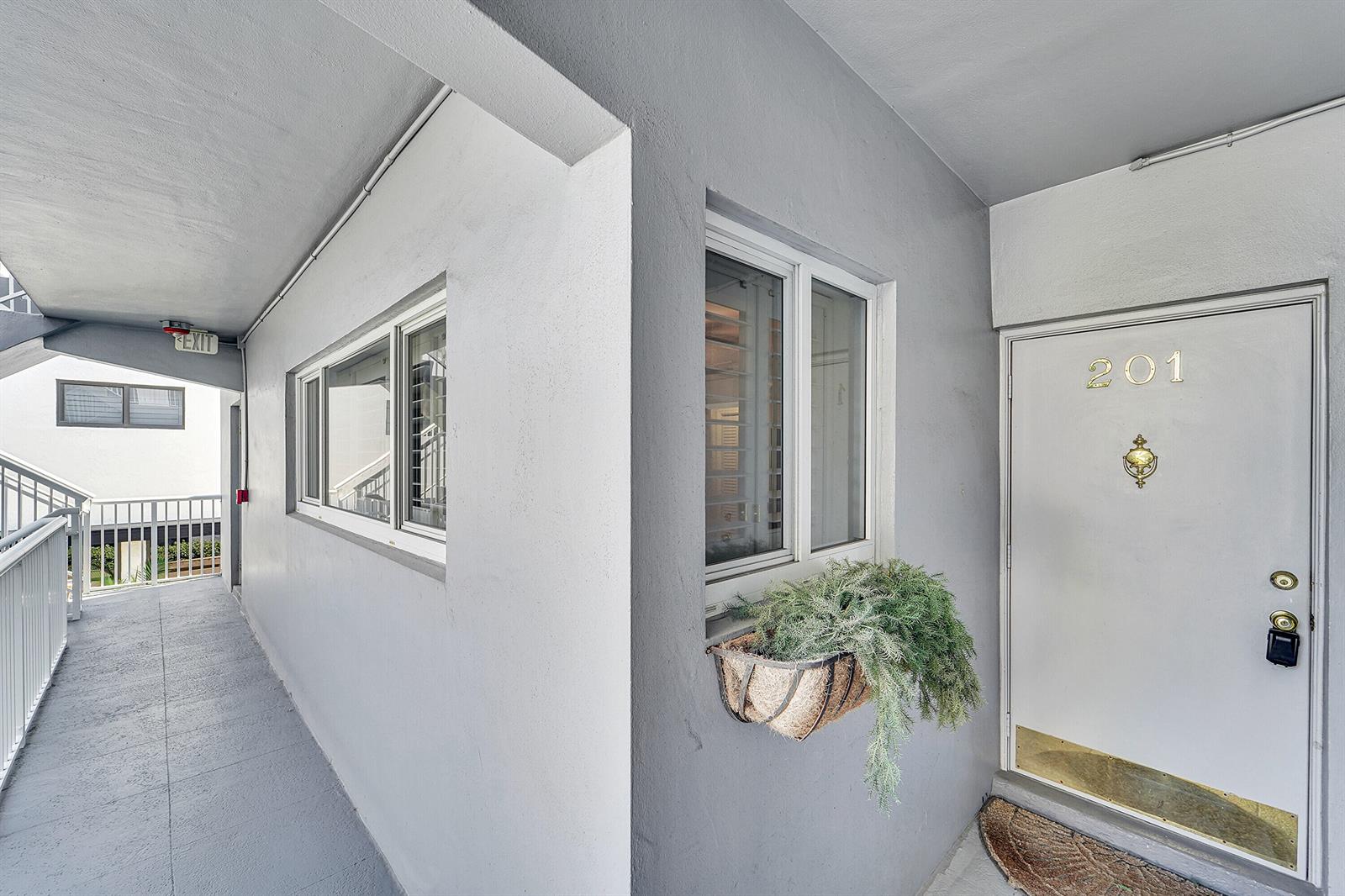 An exterior view of a building hallway featuring a door numbered 201 and windows — 1201 S Riverside Drive # 201, Pompano Beach FL 33062, POMPANO BEACH, FL