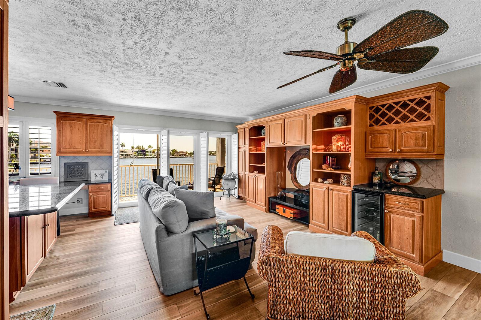 A living room features wood cabinetry, a gray sofa, a wicker chair, and waterfront views — 1201 S Riverside Drive # 201, Pompano Beach FL 33062, POMPANO BEACH, FL
