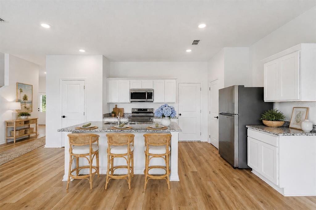 A bright kitchen features white cabinets, a granite-topped island with three stools, and wood flooring — 8700 SPORTSMAN LOOP, GROVELAND, FL