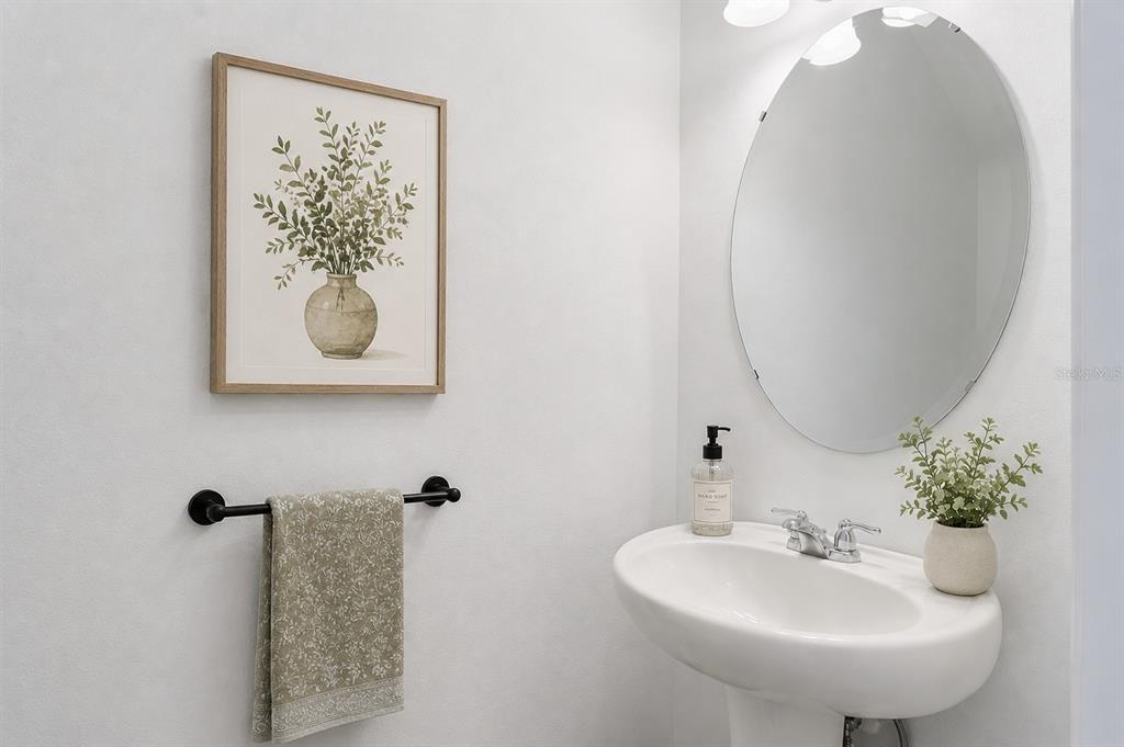 A white pedestal sink sits below an oval mirror in a minimalist bathroom — 8700 SPORTSMAN LOOP, GROVELAND, FL