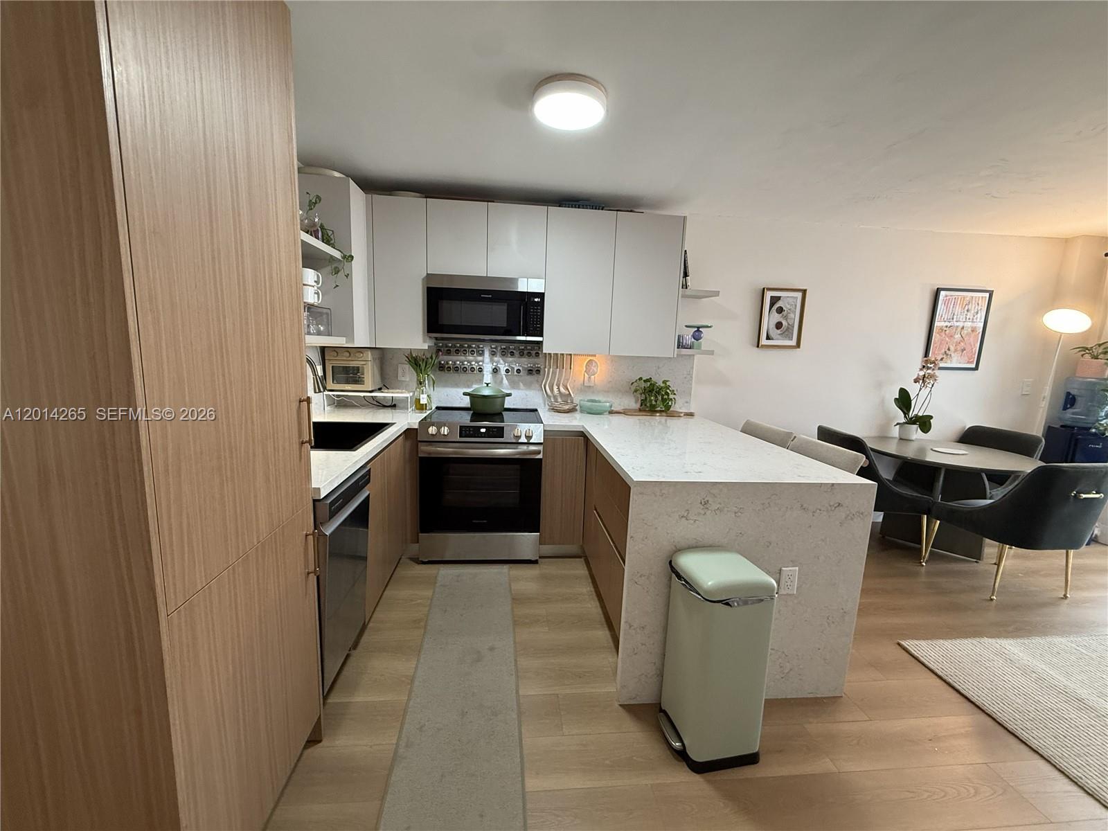 A modern kitchen features white upper cabinets, wood-tone lower cabinets, and a white quartz countertop — 1666 West Ave # 305, Miami Beach FL 33139, MIAMI BEACH, FL